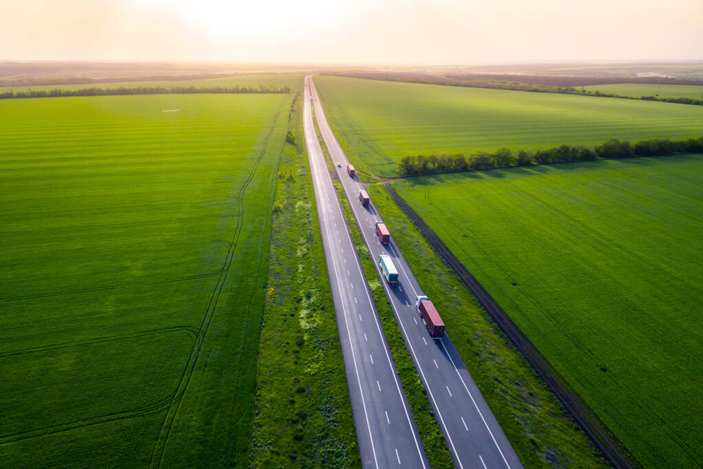 trucks on the higthway sunset. cargo delivery driving on asphalt road along the green fields. seen from the air. Aerial view landscape. drone photography.