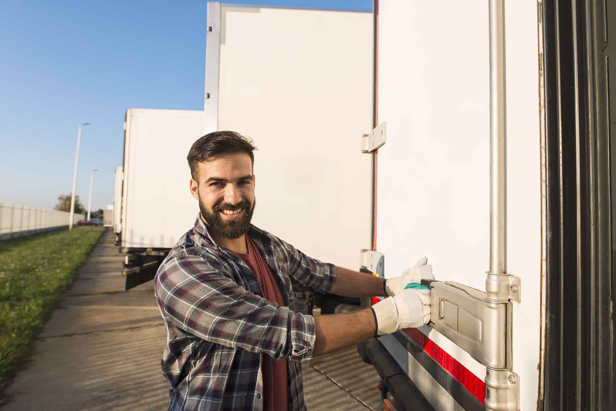 Smiling truck driver in working gloves opening or closing truck