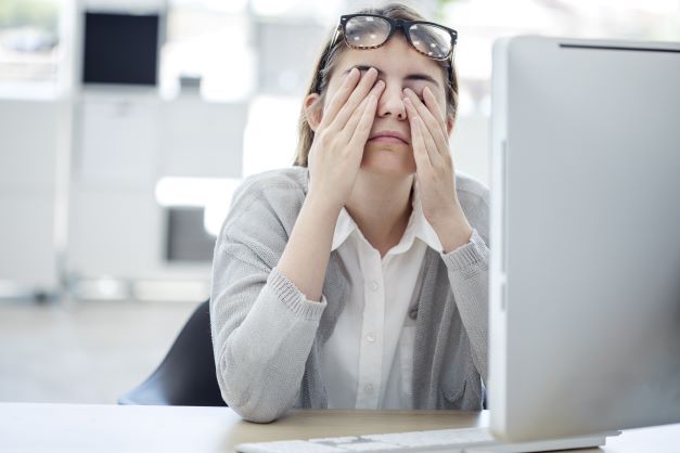Person in front of the computer covering her eyes with both hands