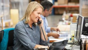 A dispatcher talking on the phone and looking at a computer in a busy office.