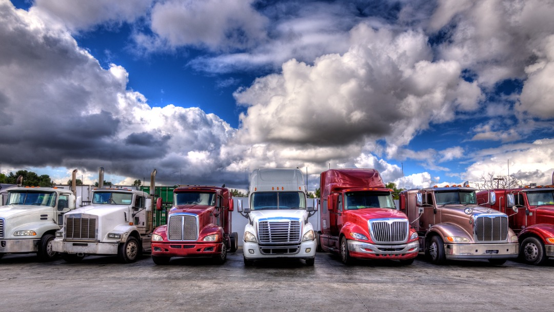 A colourful row of commercial trucks in a parking lot with clouds and blue sky.