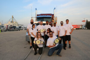 A picture of a group of people holding championship belts in front of a commercial truck.