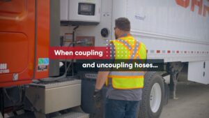 A picture of a person looking at the hoses connecting a commercial truck with the trailer.