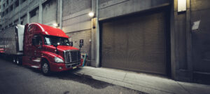 A picture of a red commercial truck with trailer parked in a back lane in the evening.